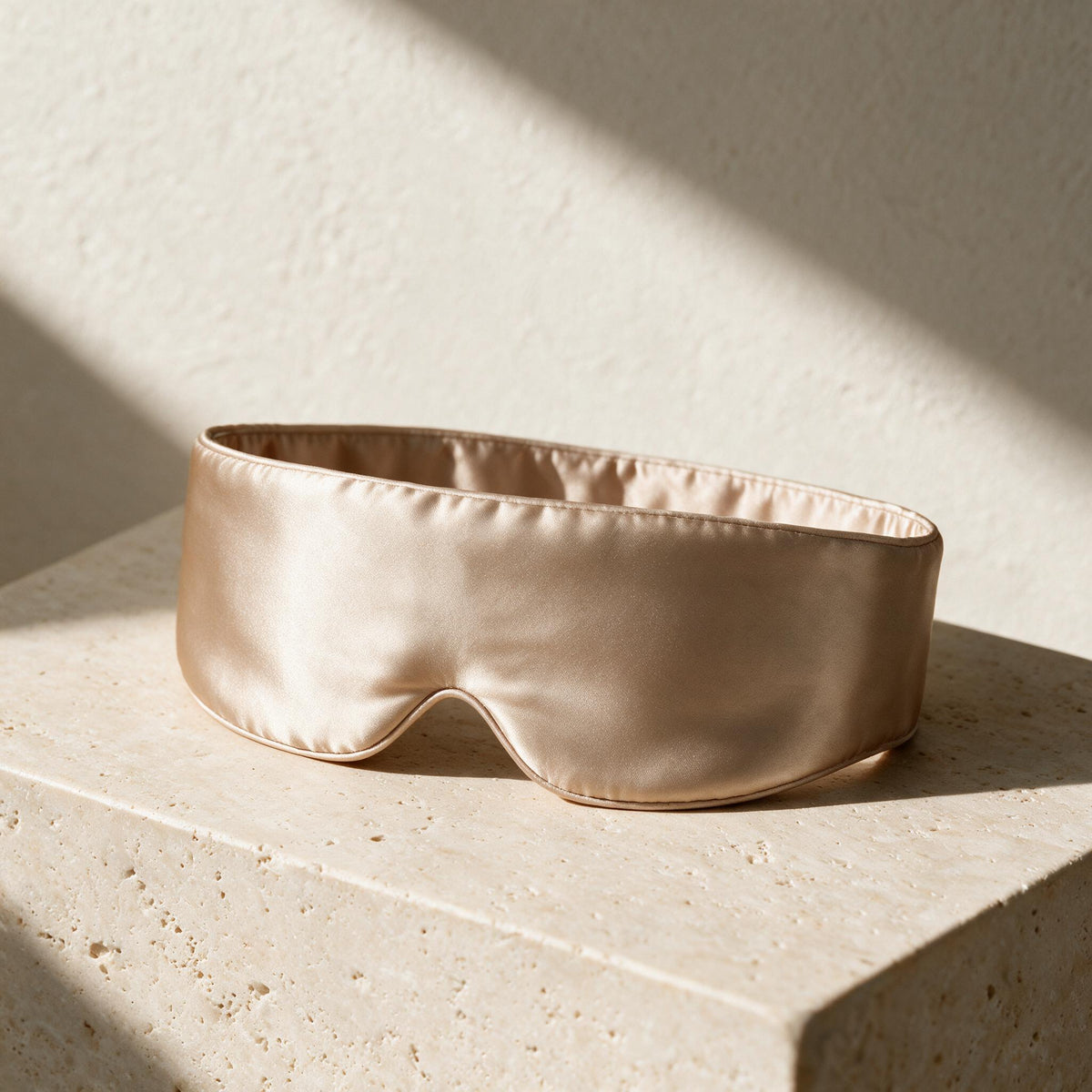 Champagne Mulberry Silk Sleep Mask in its wide wraparound shape on travertine.